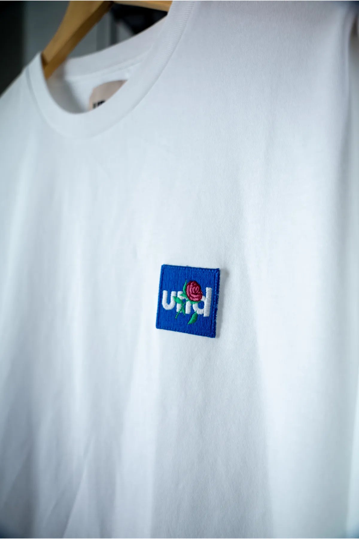 Und white T-shirt with "Und Rose Embroidery in Blue Badge"