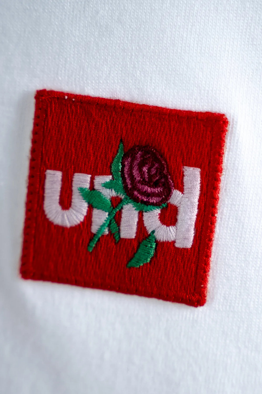Und white T-shirt with "Und Rose Embroidery in Red Badge"